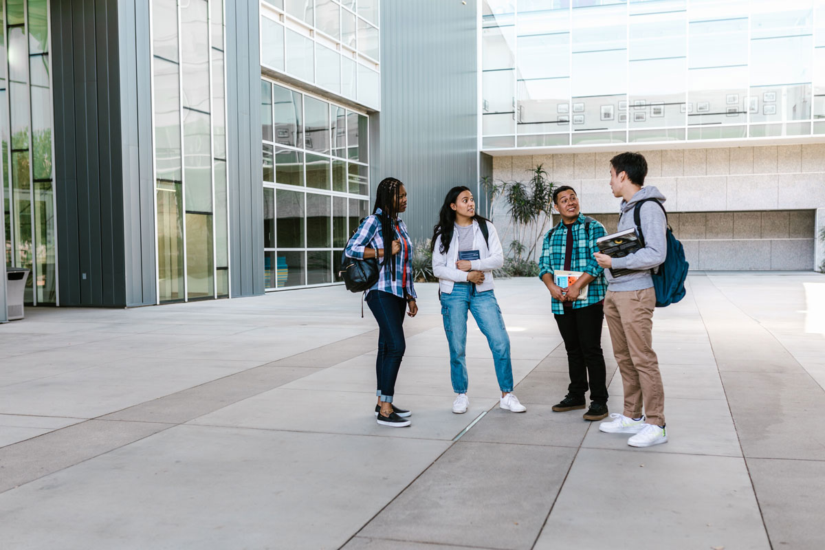 A diverse group of students talking outside a modern campus building, representing youth engagement and inclusion